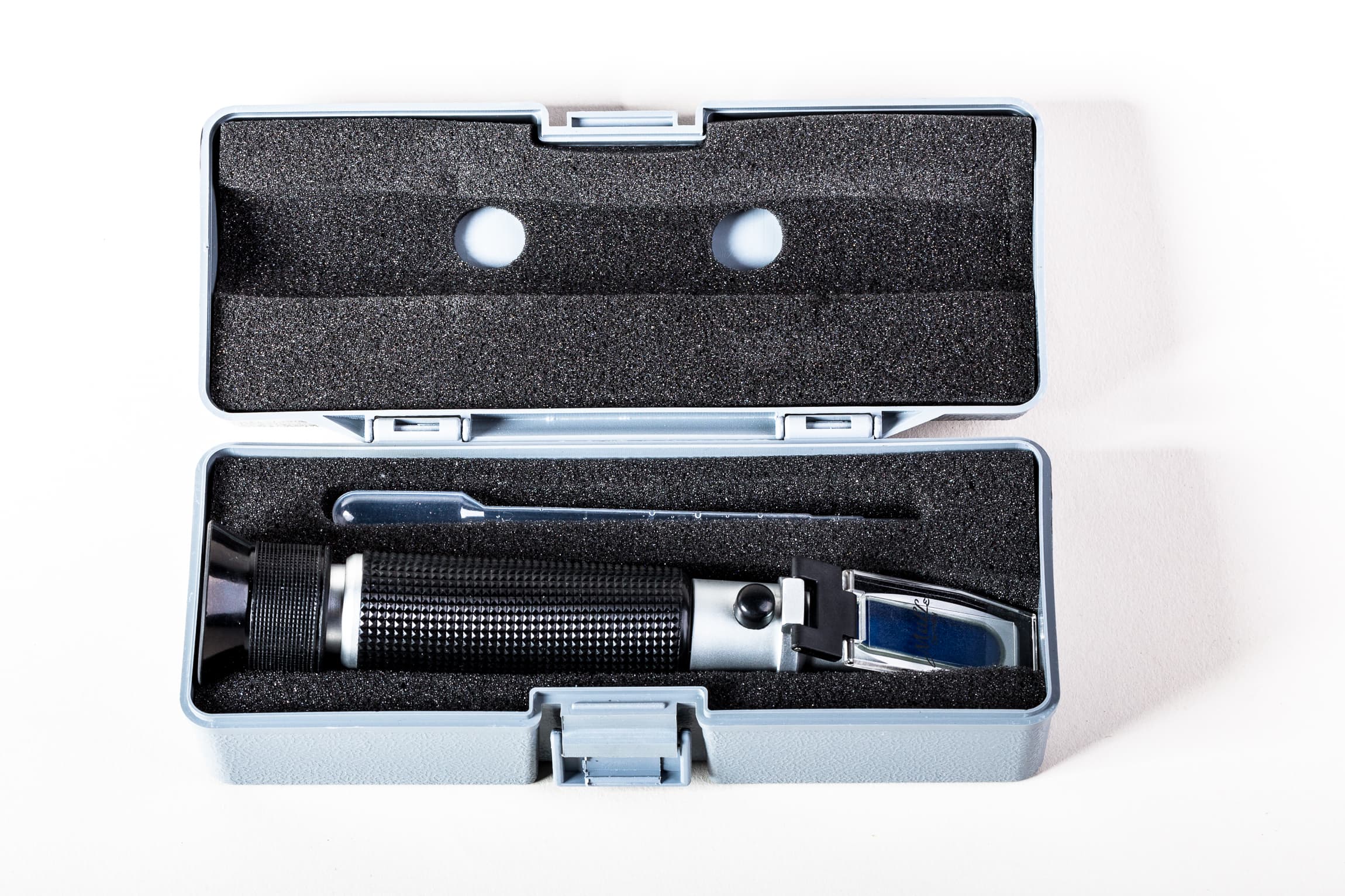 Handheld salinity refractometer with ATC in an open hard case beside a plastic pipette