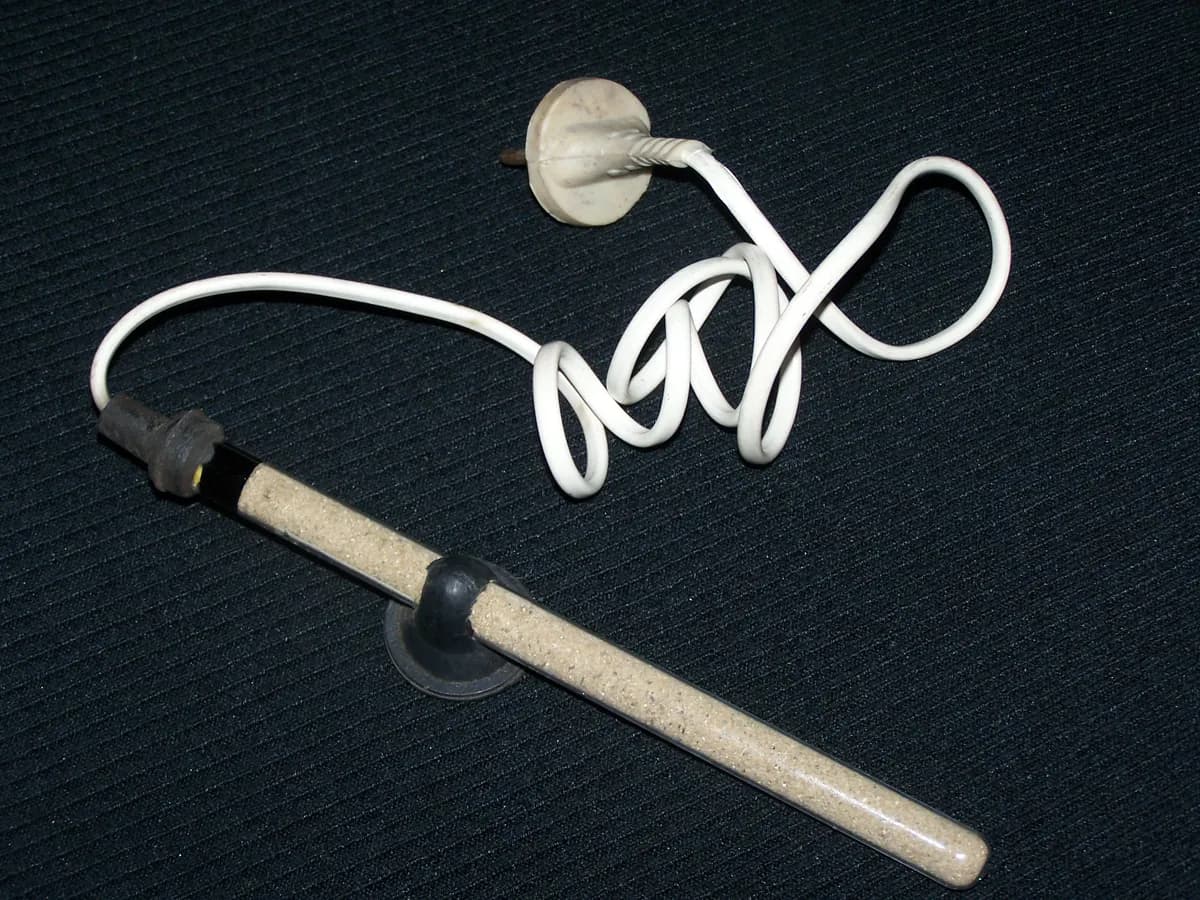 Glass-tube submersible aquarium heater with suction cup and power cord on a dark surface