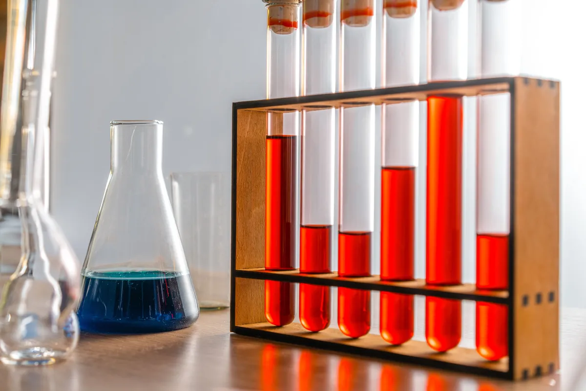 Glass test tubes with colored liquid samples in a wooden rack beside lab glassware โ liquid water testing