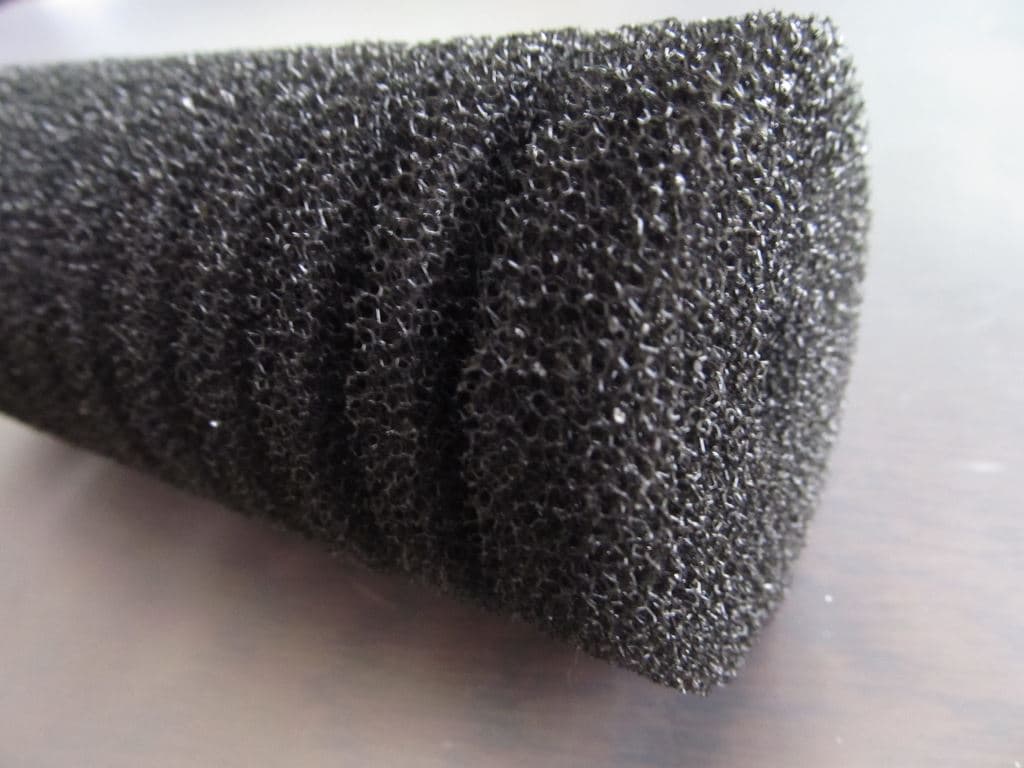 Coarse foam cylinder from an aquarium sponge filter on a plain background