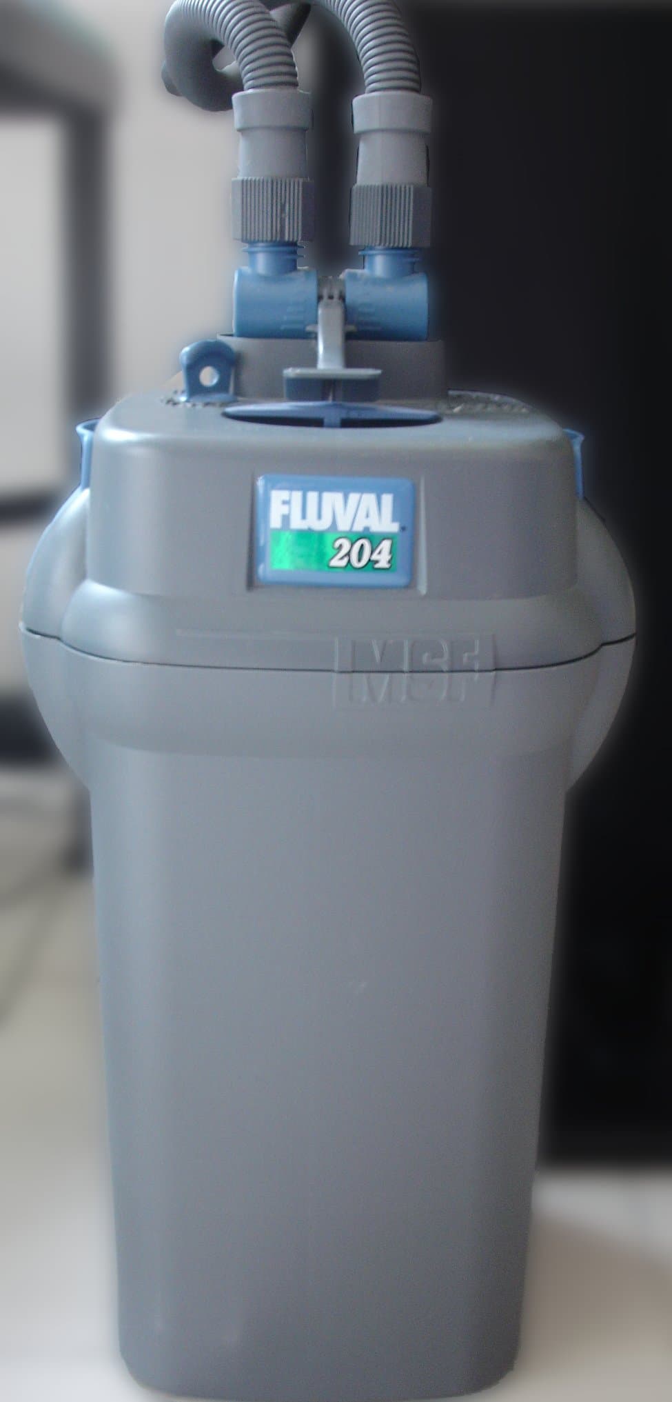 External aquarium canister filter standing beside a glass tank with intake and return hoses